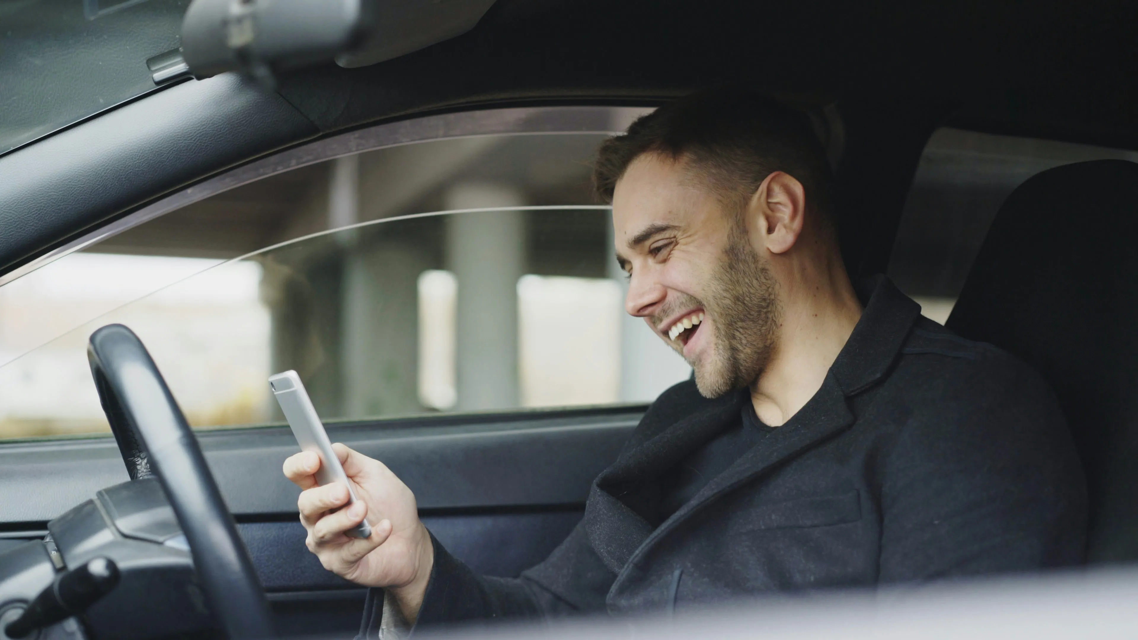 Conductor sonriendo dentro de su auto mientras agenda su lavado desde el celular